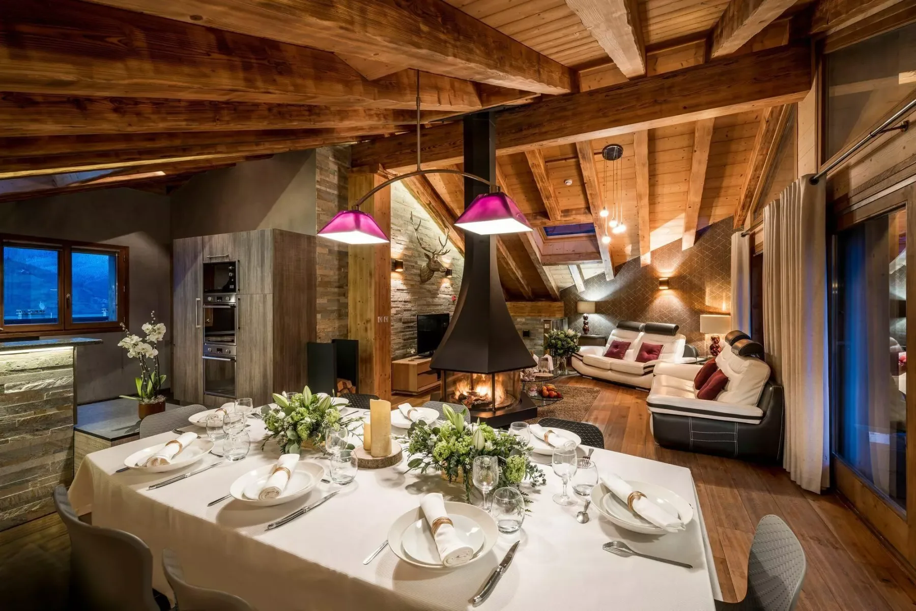 A dining area and lounge beneath exposed wooden beams, with a table and fireplace.