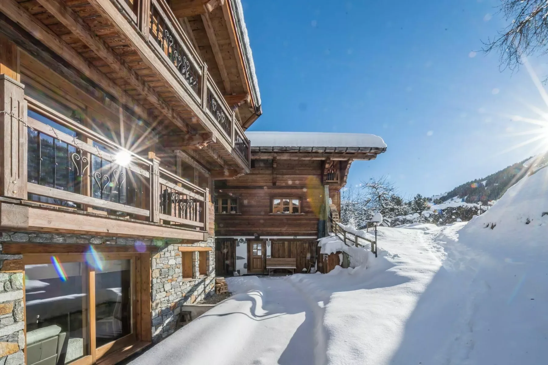 A wooden chalet stands beside a snow-covered slope under a clear blue sky.