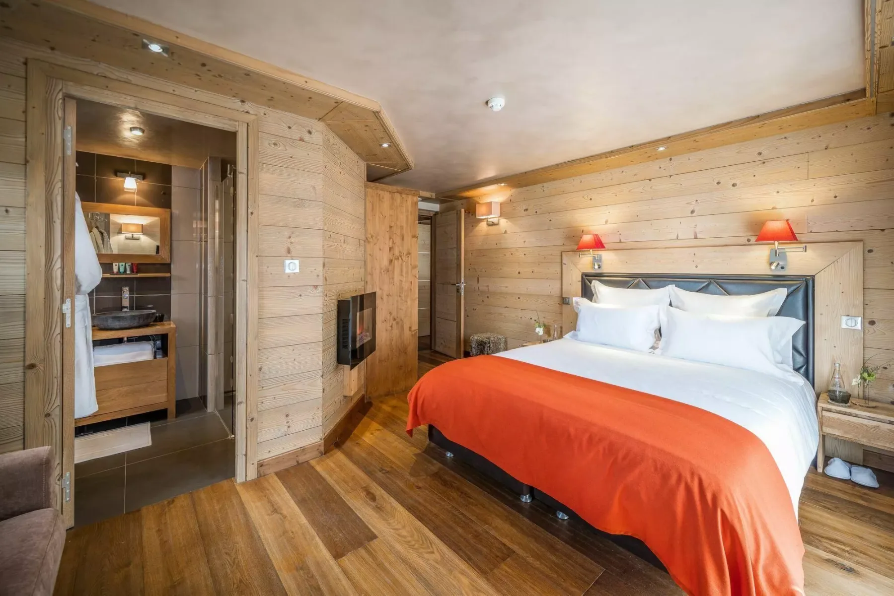 A wood-paneled bedroom with a bed dressed in white linens and an orange cover.