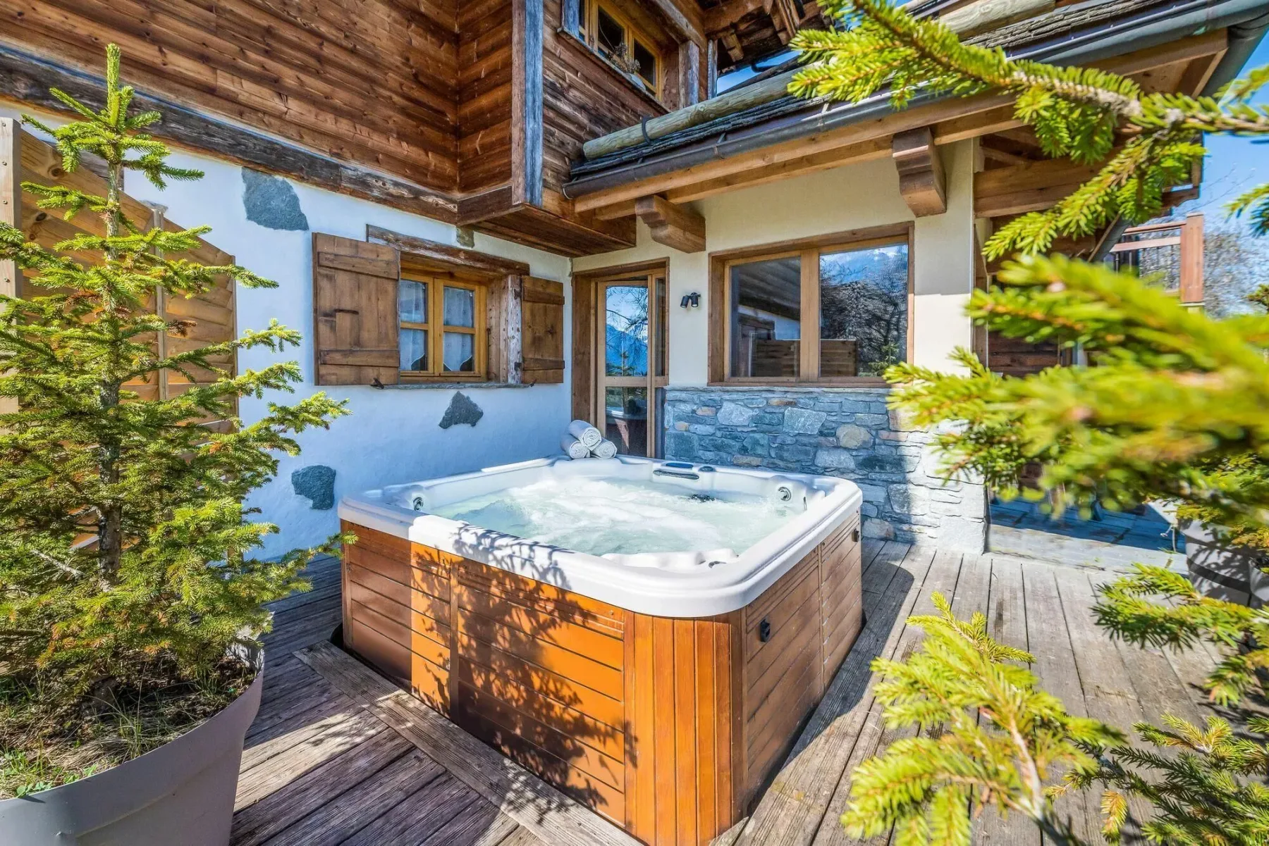 An outdoor hot tub sits on a wooden deck beside a chalet-style building.