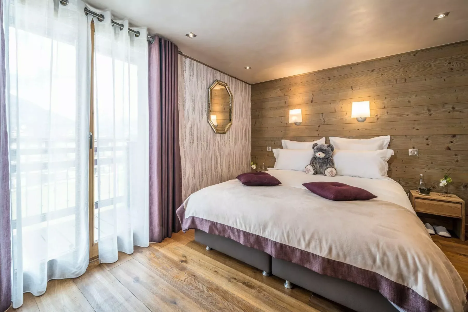 A bedroom with a neatly made bed and tall curtained windows.