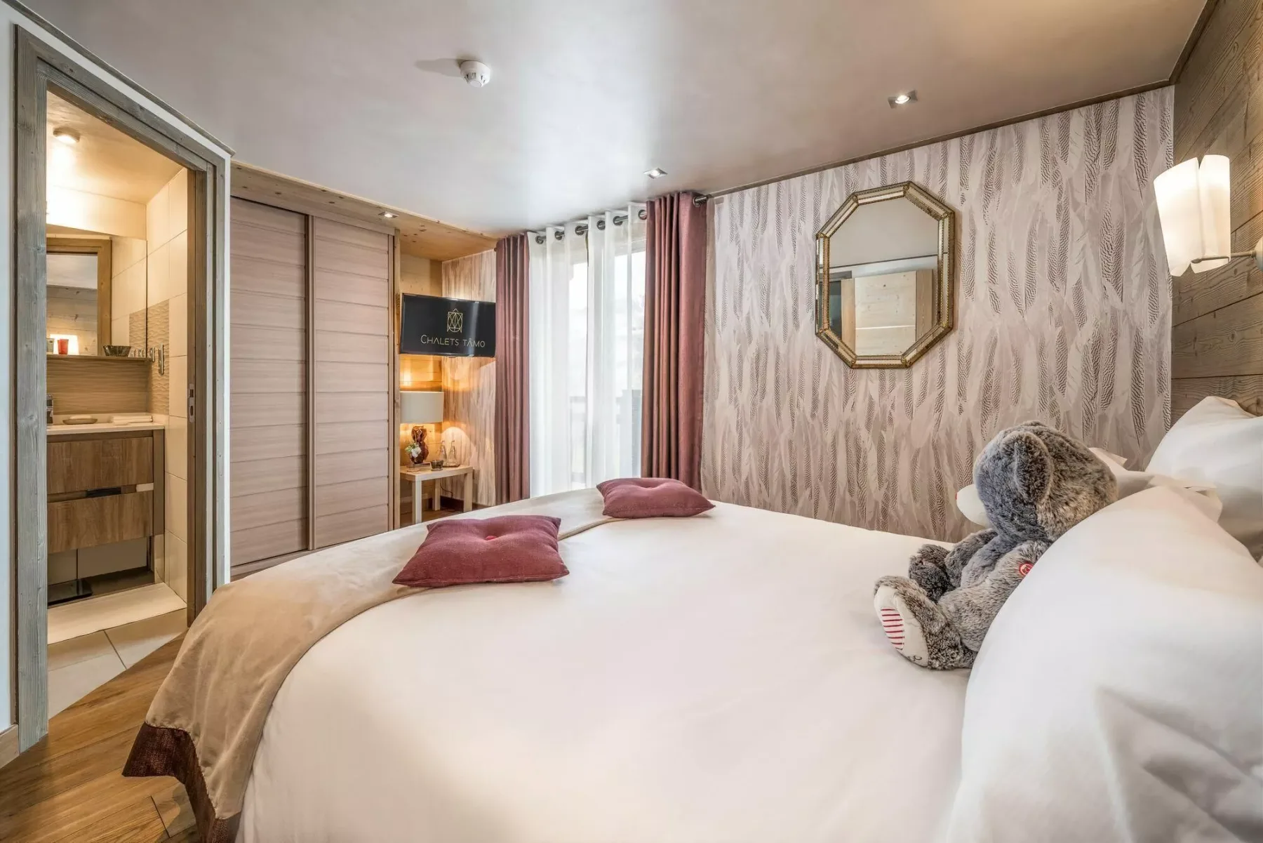 A bedroom with a large bed, patterned wallpaper, and a mirrored wall decoration.