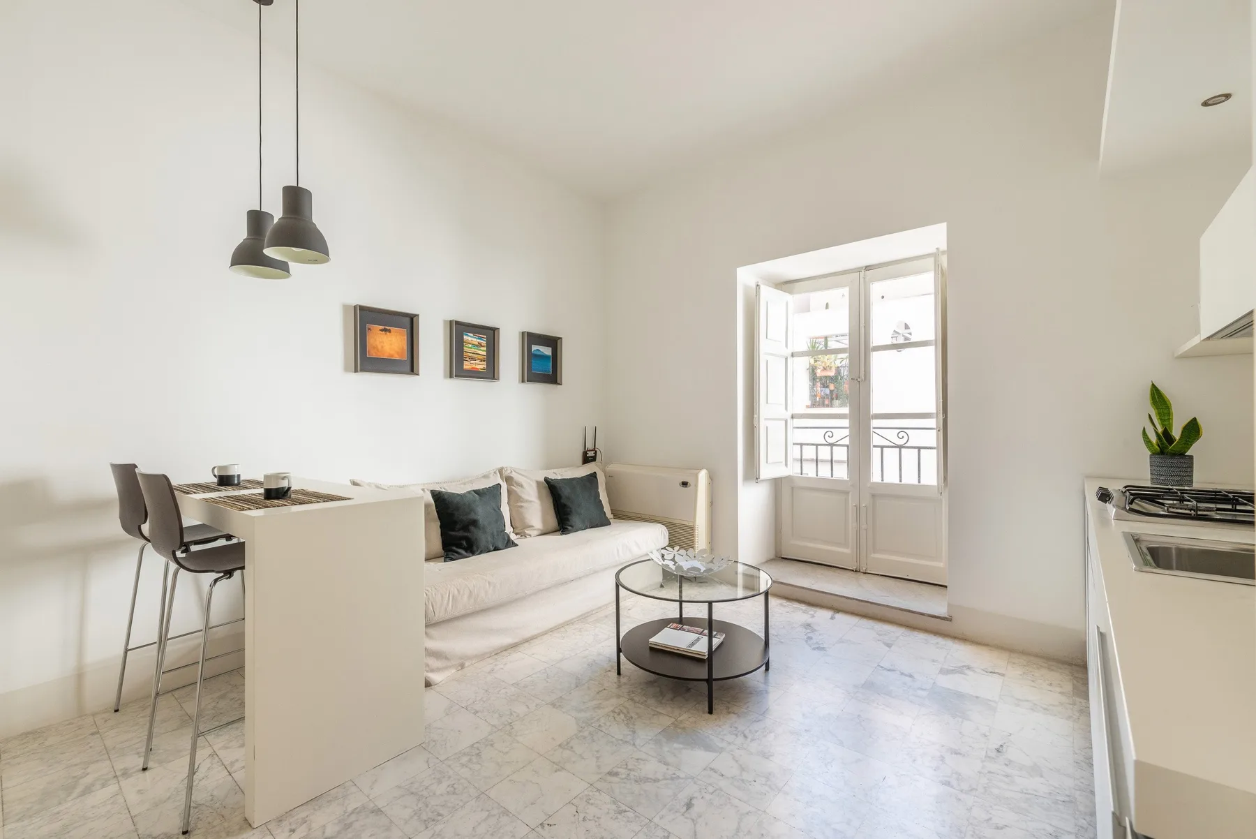 Una sala luminosa con sofá, barra de comedor y mesa de centro de vidrio.