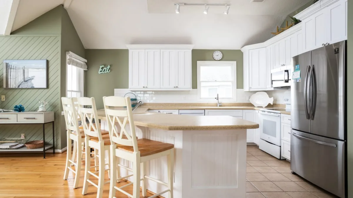 Una cocina luminosa con gabinetes blancos, una isla central y asientos de barra.