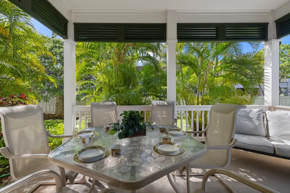 Comedor exterior cubierto con una mesa puesta y asientos frente a vegetación tropical.
