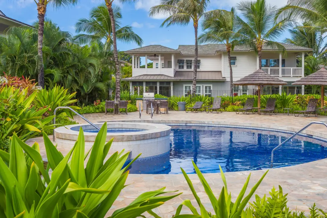 Una piscina al aire libre está frente a una casa rodeada de palmeras y vegetación.