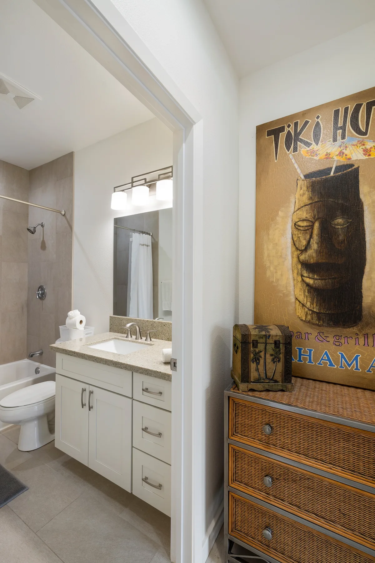 Un baño con lavabo e inodoro junto a una cómoda con una imagen tiki encima.
