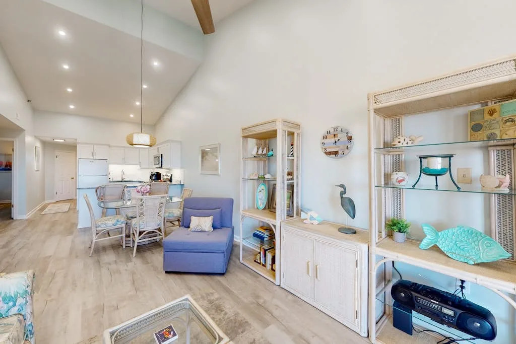A bright living and dining area with seating, shelving, and a table.