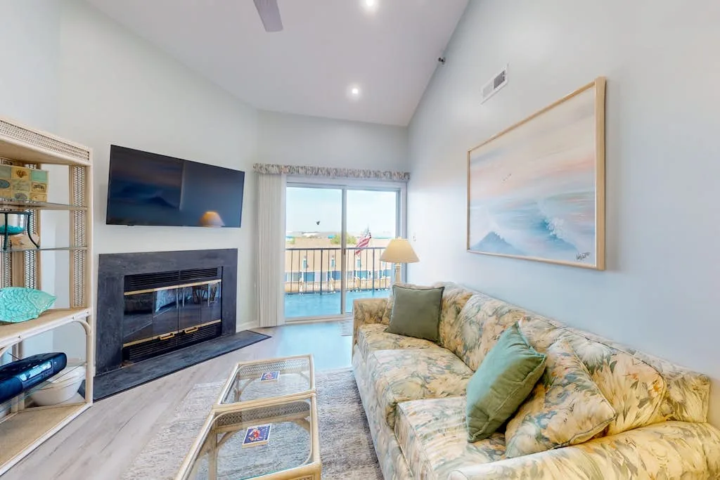 A bright living room with a floral sofa and sliding glass doors opening to a balcony.