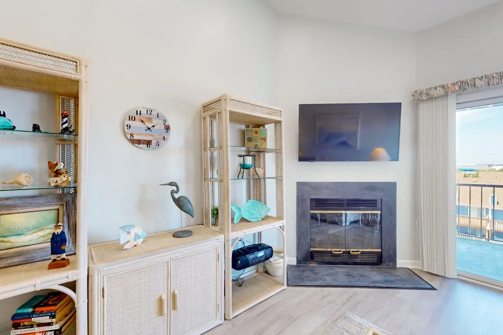 A bright living room features a fireplace, display shelves, and a glass door opening onto a balcony.