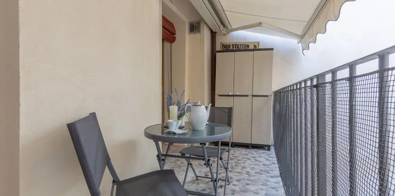 Un balcón cubierto tiene una mesa pequeña y sillas junto a una barandilla metálica.