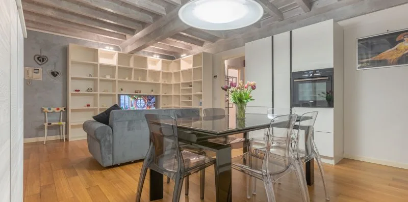 An open-plan living and dining area with shelving, seating, and a glass dining table.