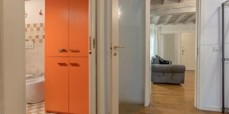 A hallway opens onto a living area, with an orange cabinet beside the bathroom.