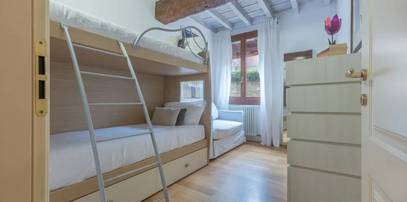 Un dormitorio con una litera y una ventana con cortinas transparentes.