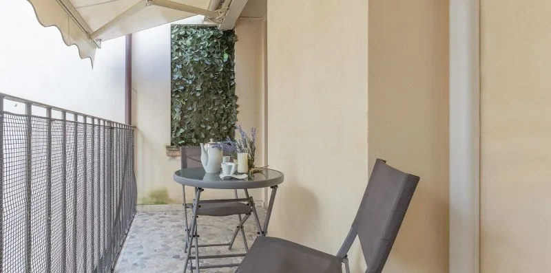 Un pequeño patio con una mesa, asientos y un panel de pared cubierto de hojas.