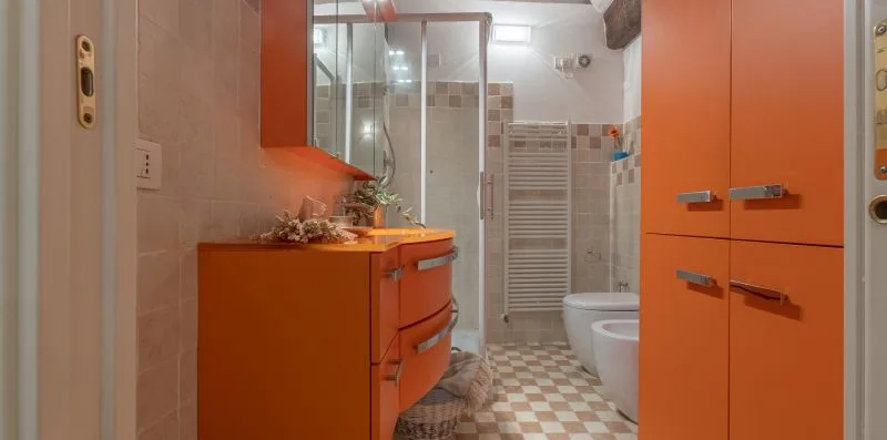 A bathroom with orange cabinets and a glass shower enclosure.