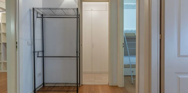 Un pasillo con un perchero abierto y una puerta hacia un dormitorio.