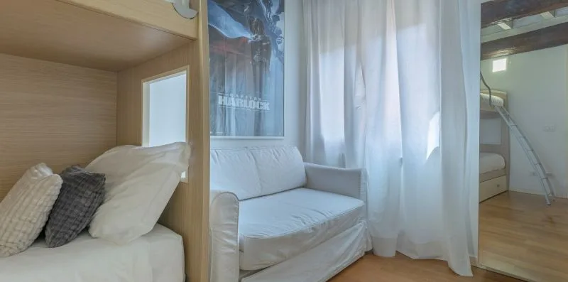 Una pequeña zona para dormir con una cama, un sofá y cortinas blancas.