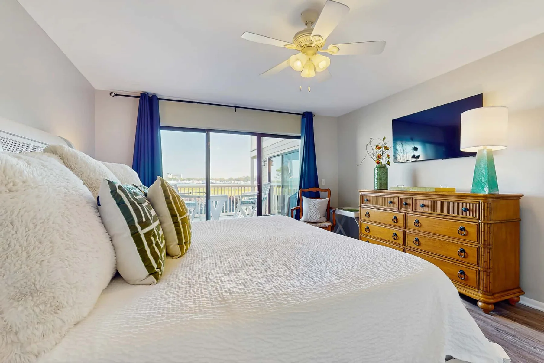 A bedroom with a large bed, blue curtains, and a dresser beside the window.