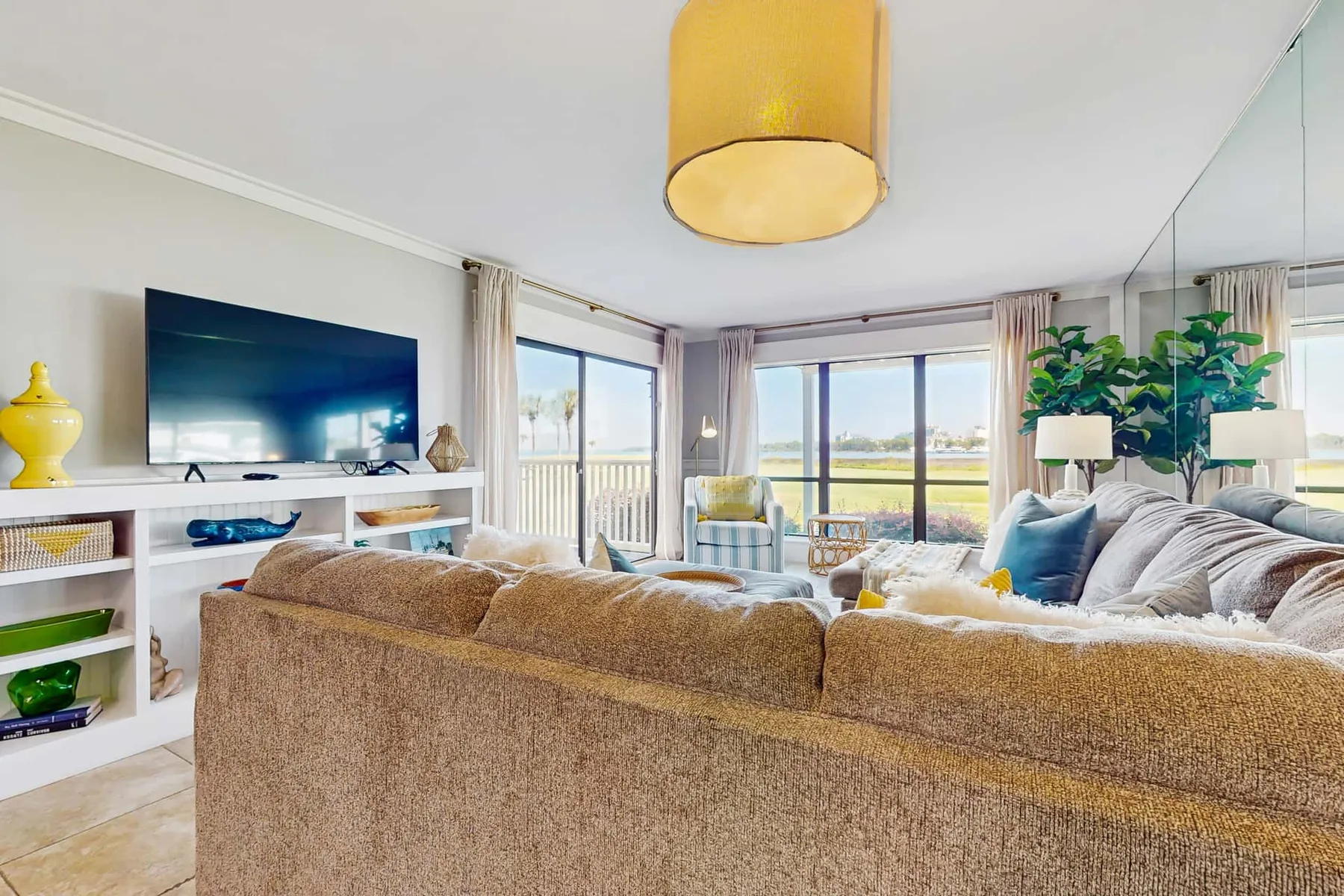 Bright living room with seating facing a television and large windows.