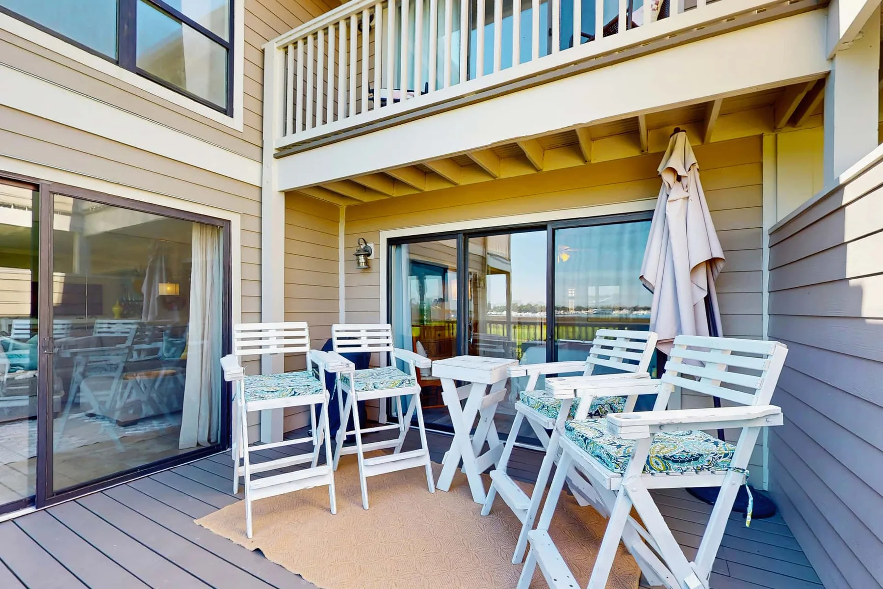 An outdoor deck with white seating, a table, and a closed umbrella.