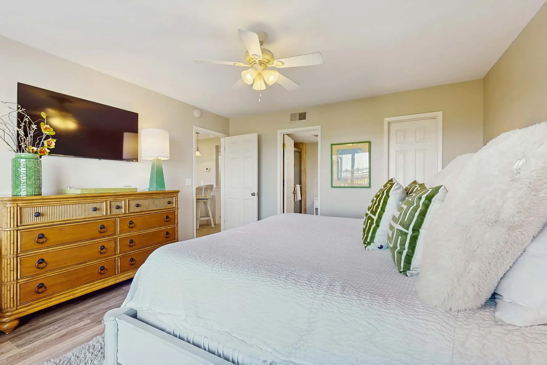 A bedroom with a large bed, wooden dresser, and ceiling fan.