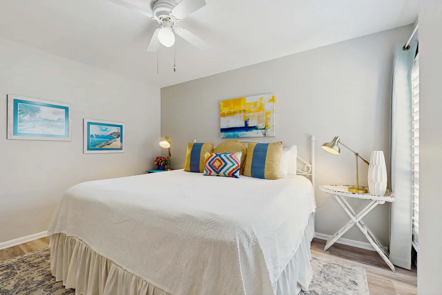 A bright bedroom with a neatly made bed and colorful artwork on the walls.