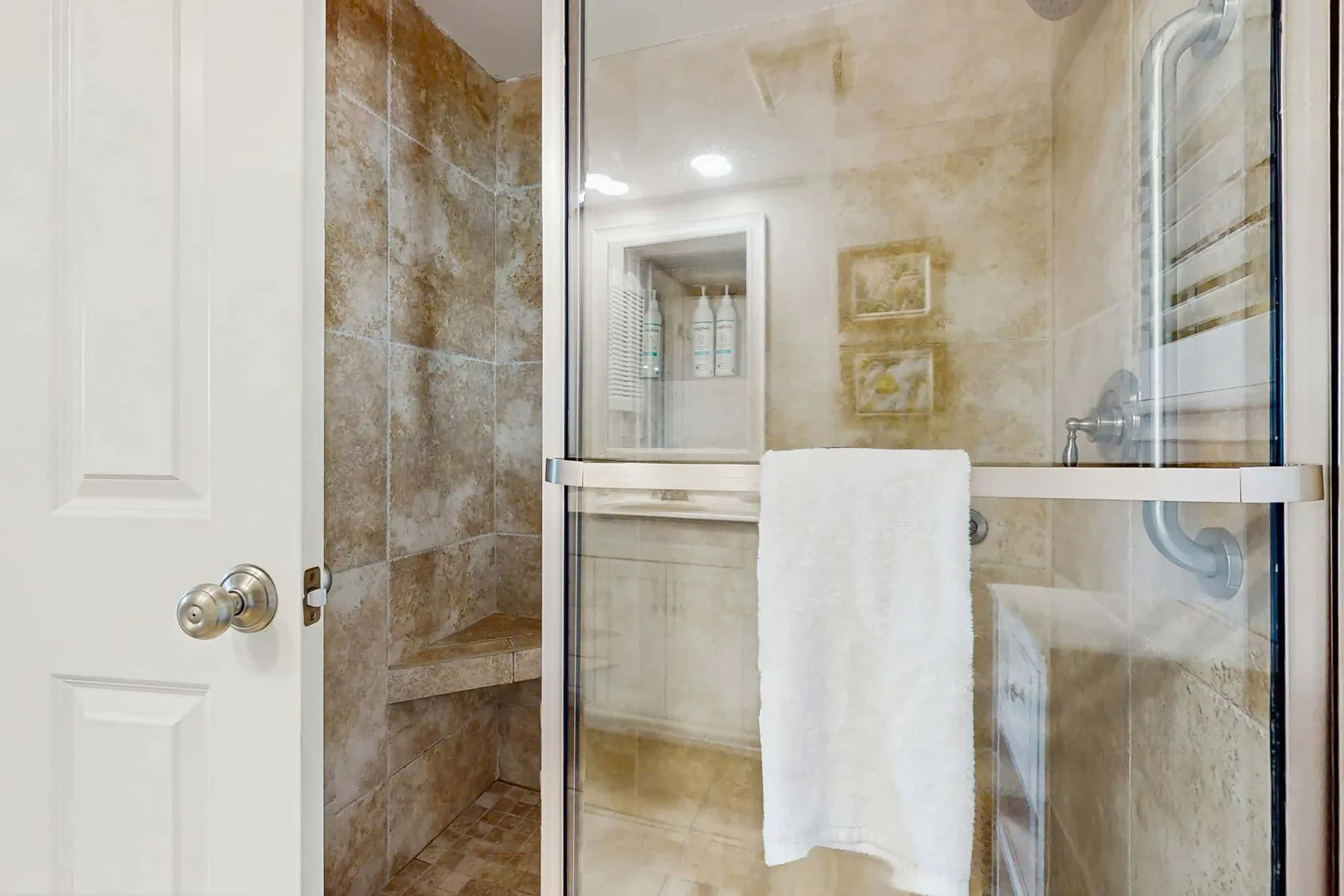 A tiled bathroom with a glass shower enclosure and a towel hanging over the rail.