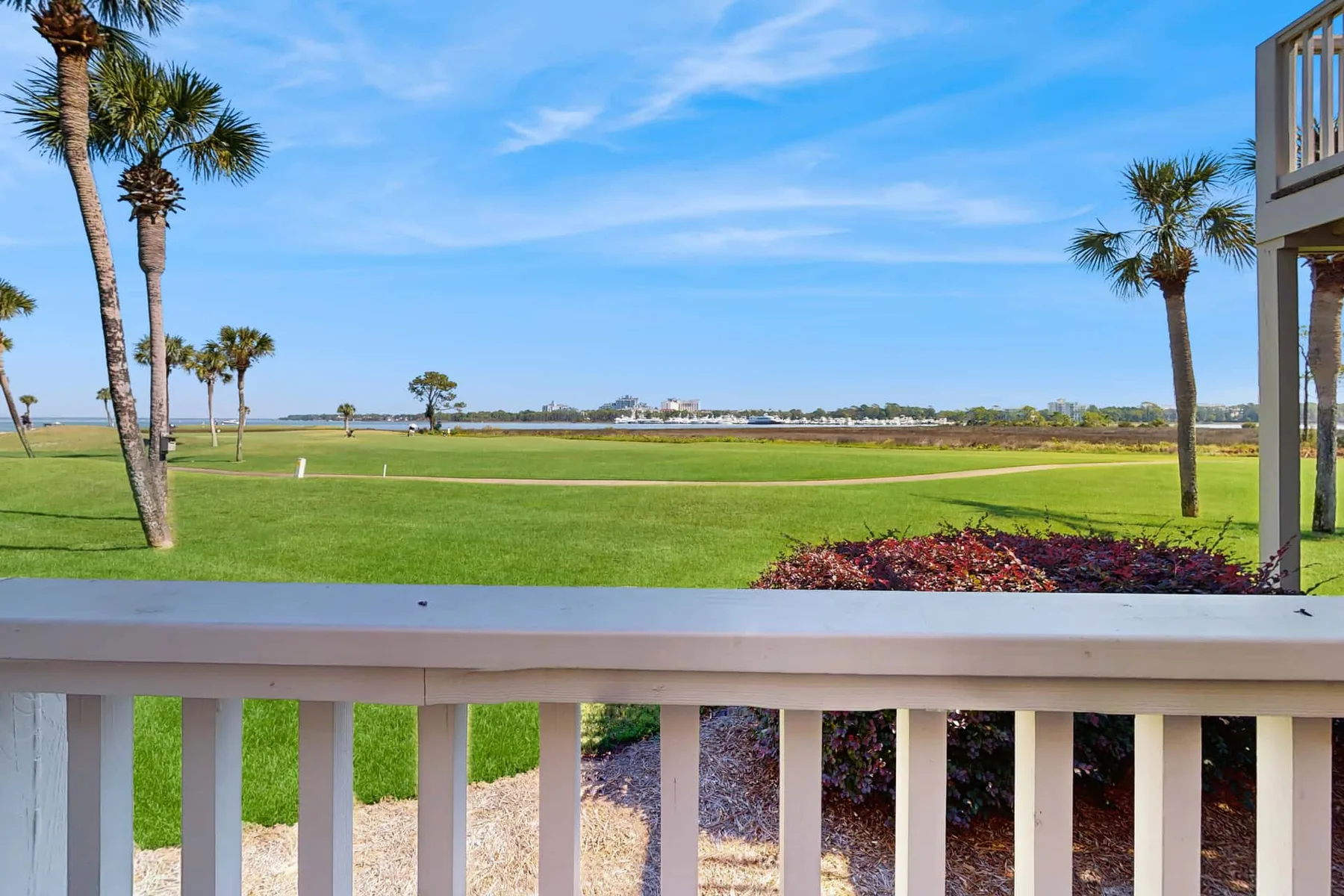 A green lawn with palm trees stretches toward the water under a blue sky.