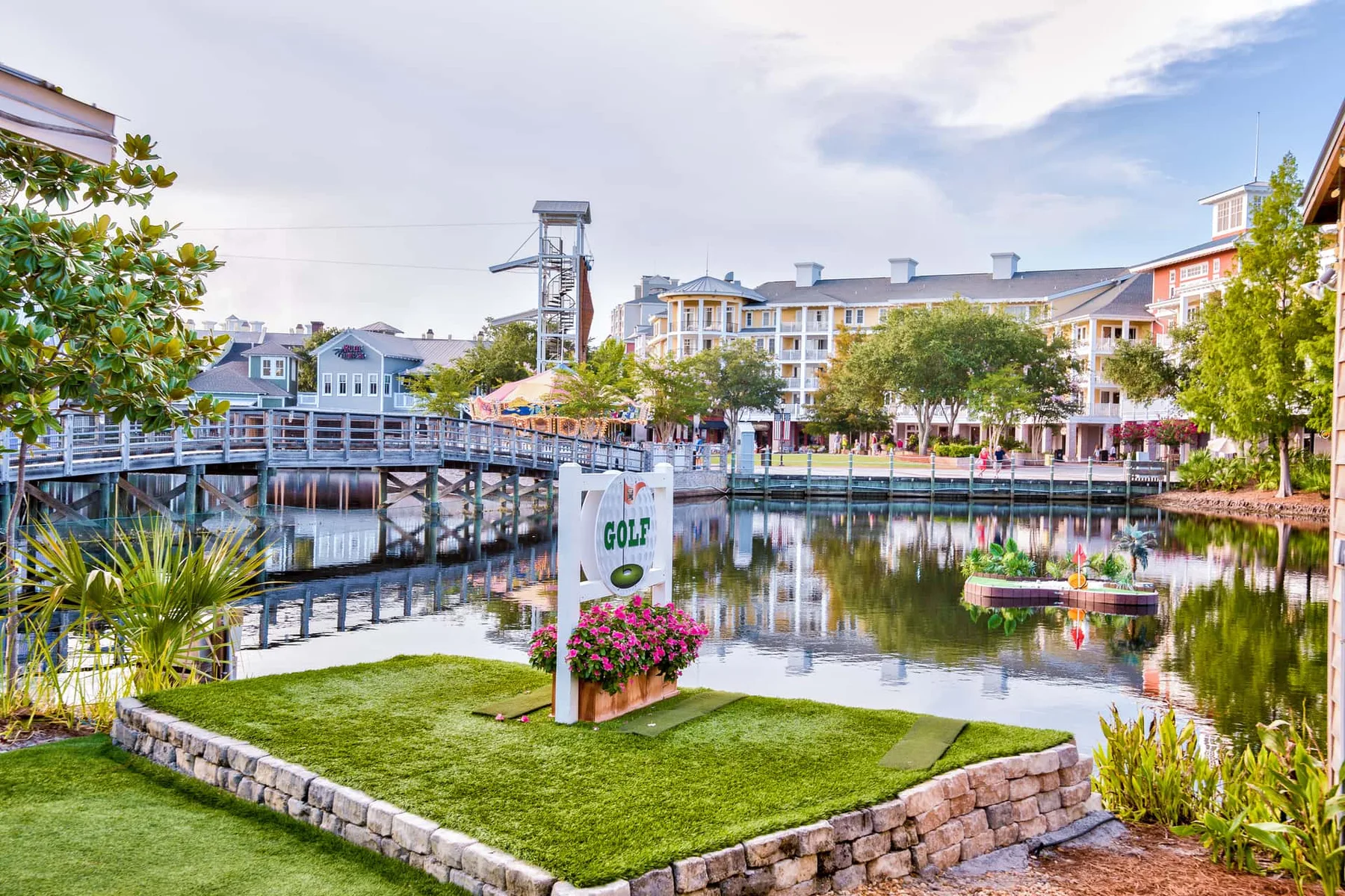A landscaped pond with a wooden walkway and colorful buildings in the background.