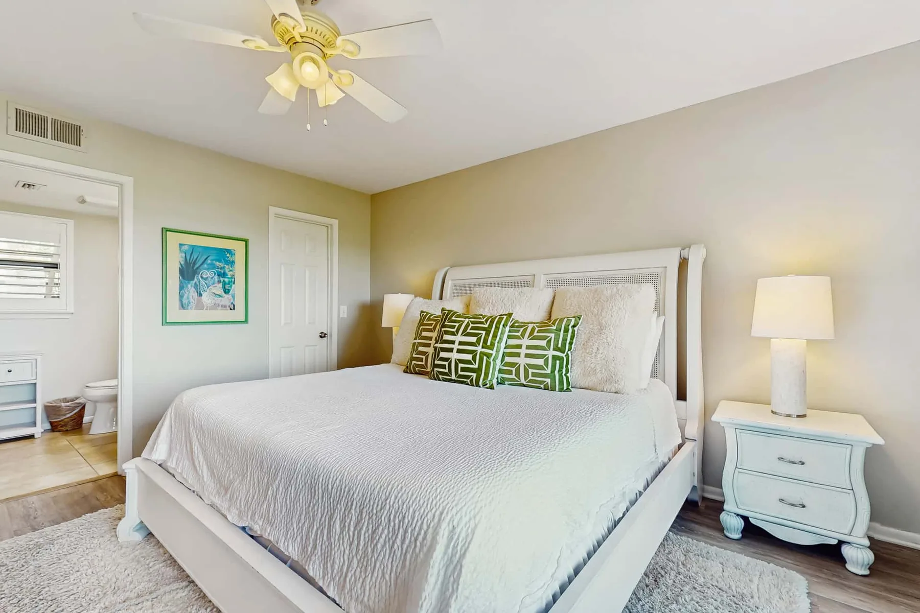 A bedroom with a large bed, patterned pillows, and a ceiling fan.