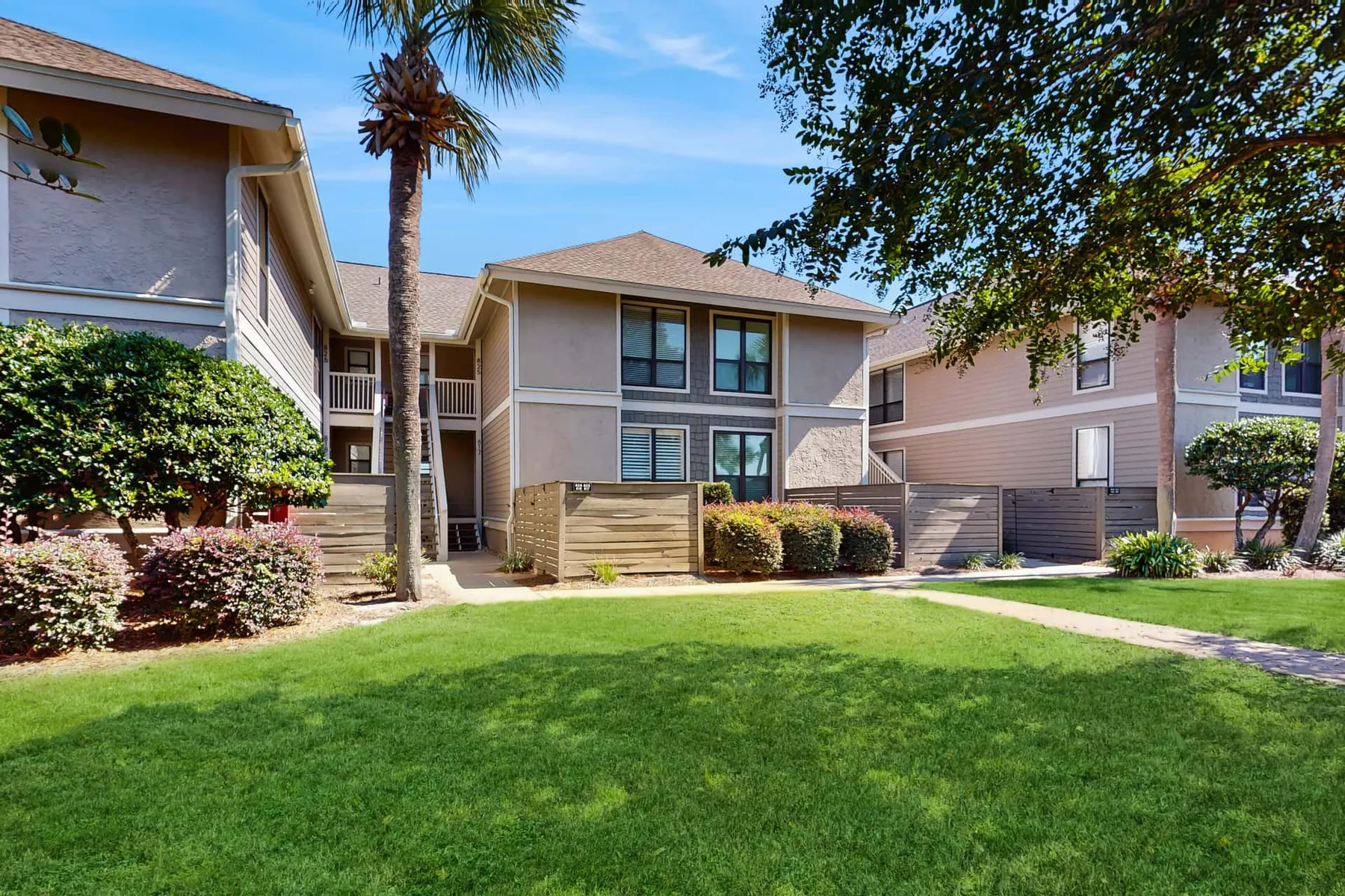 An apartment building faces a grassy courtyard with shrubs and trees.