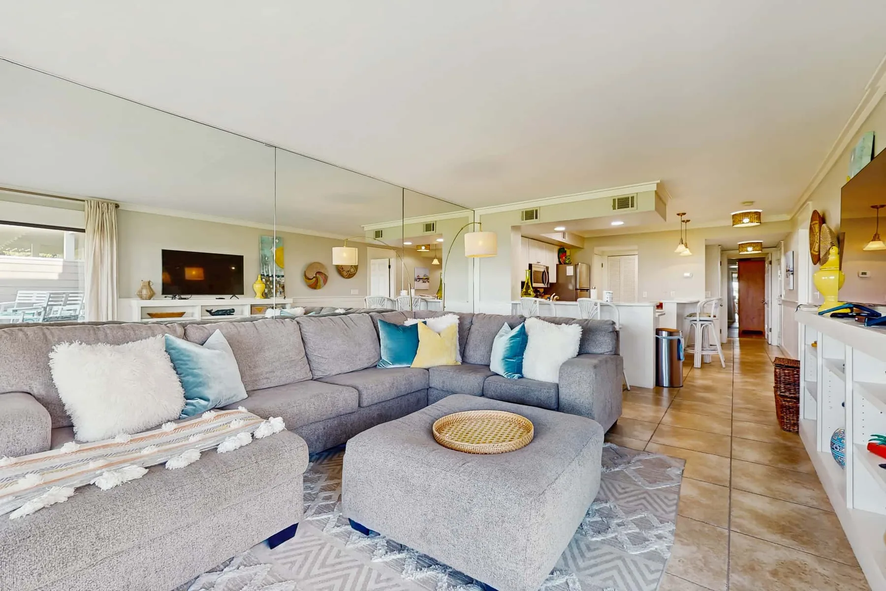 A bright living room with gray seating, a large mirror, and an open kitchen.