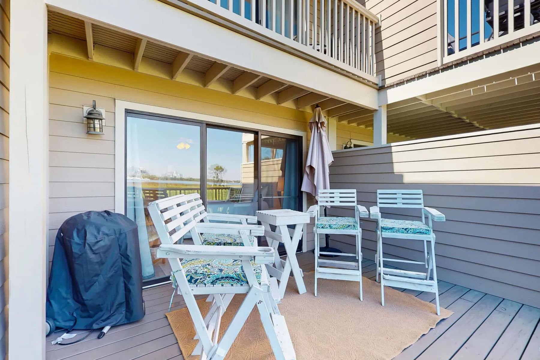 A furnished outdoor deck with white seating beside sliding glass doors.