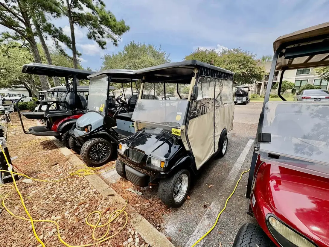 Several golf carts are parked outdoors beside a paved area.