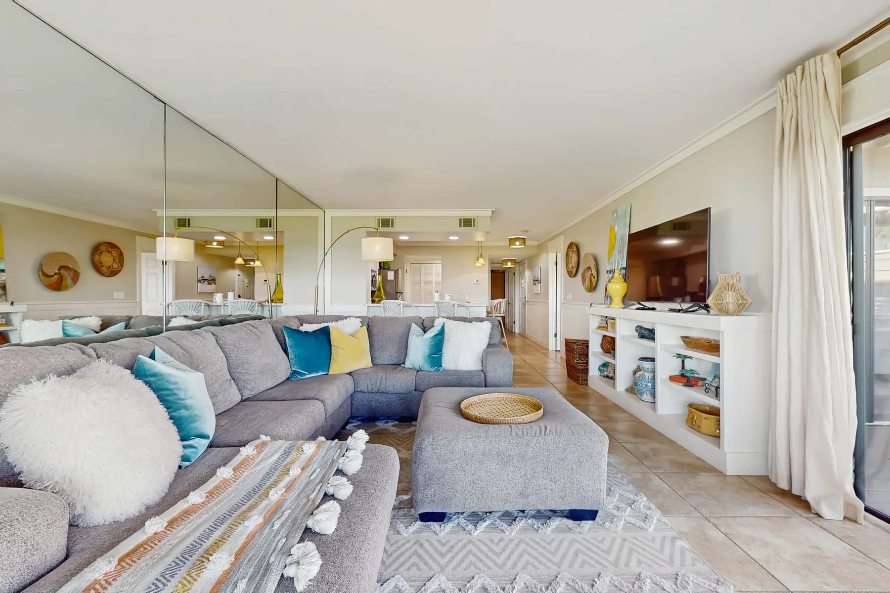 A bright living room with gray seating, a television, and a mirrored wall.