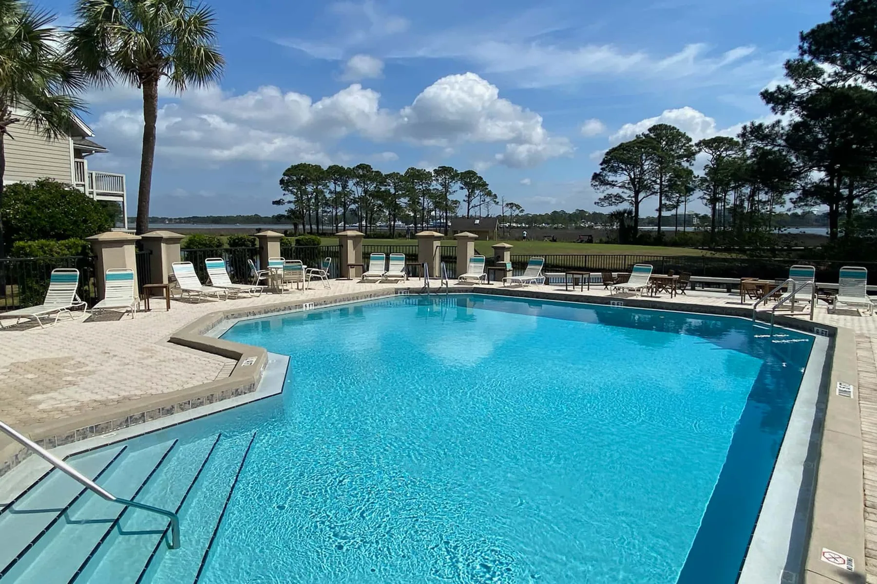 An outdoor swimming pool with lounge seating and trees in the background.