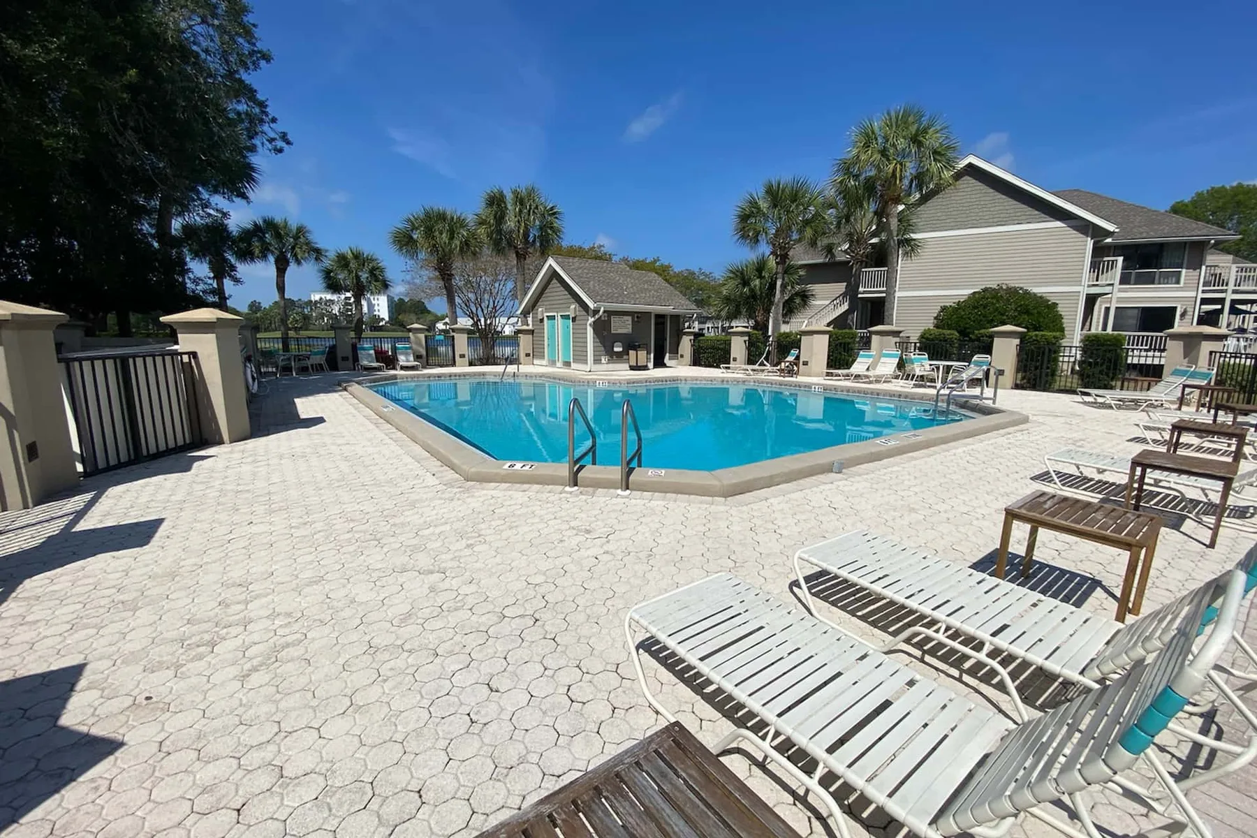 An outdoor swimming pool is surrounded by paved deck space and lounge chairs.