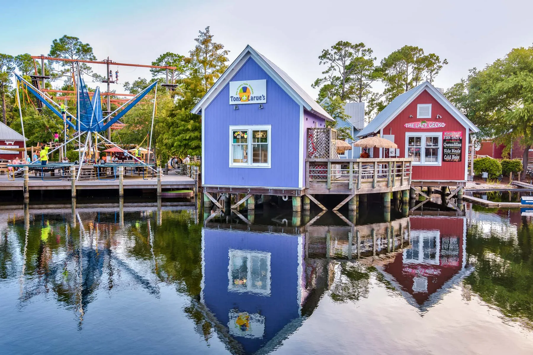 Colorful waterfront buildings and a ride sit beside calm water.