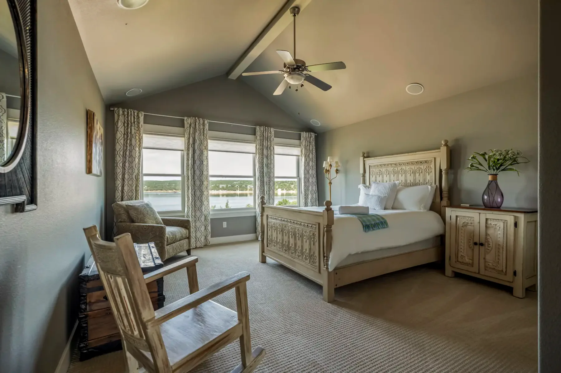 A bedroom with a carved wooden bed, seating, and windows overlooking water.