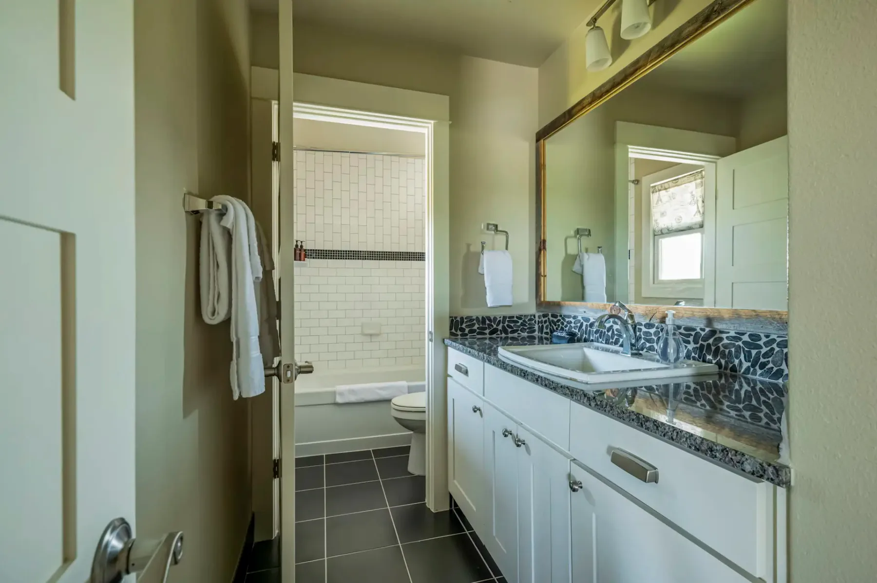 Modern bathroom with white cabinetry, black countertop, vessel sink, large mirror, and open door leading to tiled shower area.
