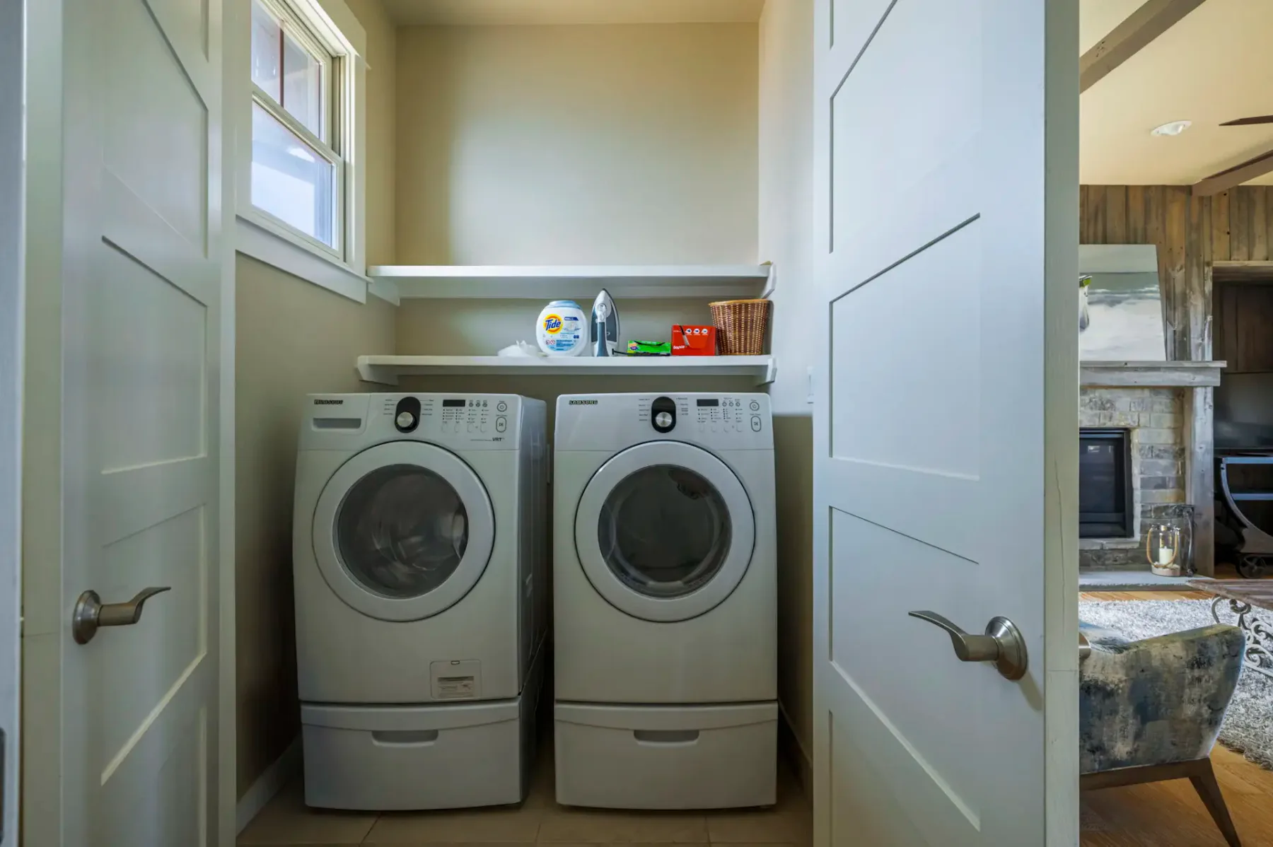 A laundry room with a washer and dryer beneath shelves holding laundry supplies.