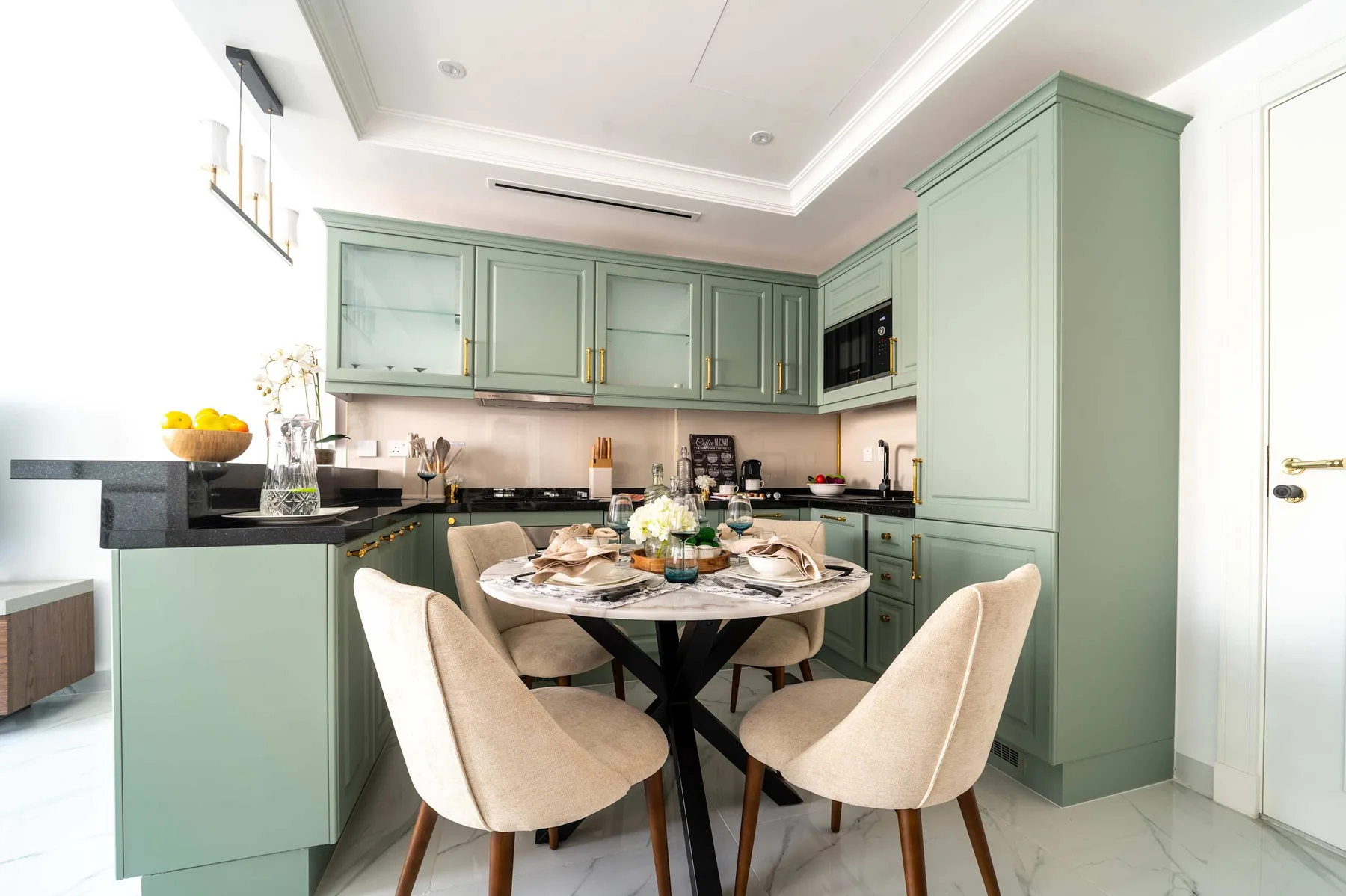 Una mesa de comedor con asientos tapizados está en una cocina luminosa con gabinetes verdes.