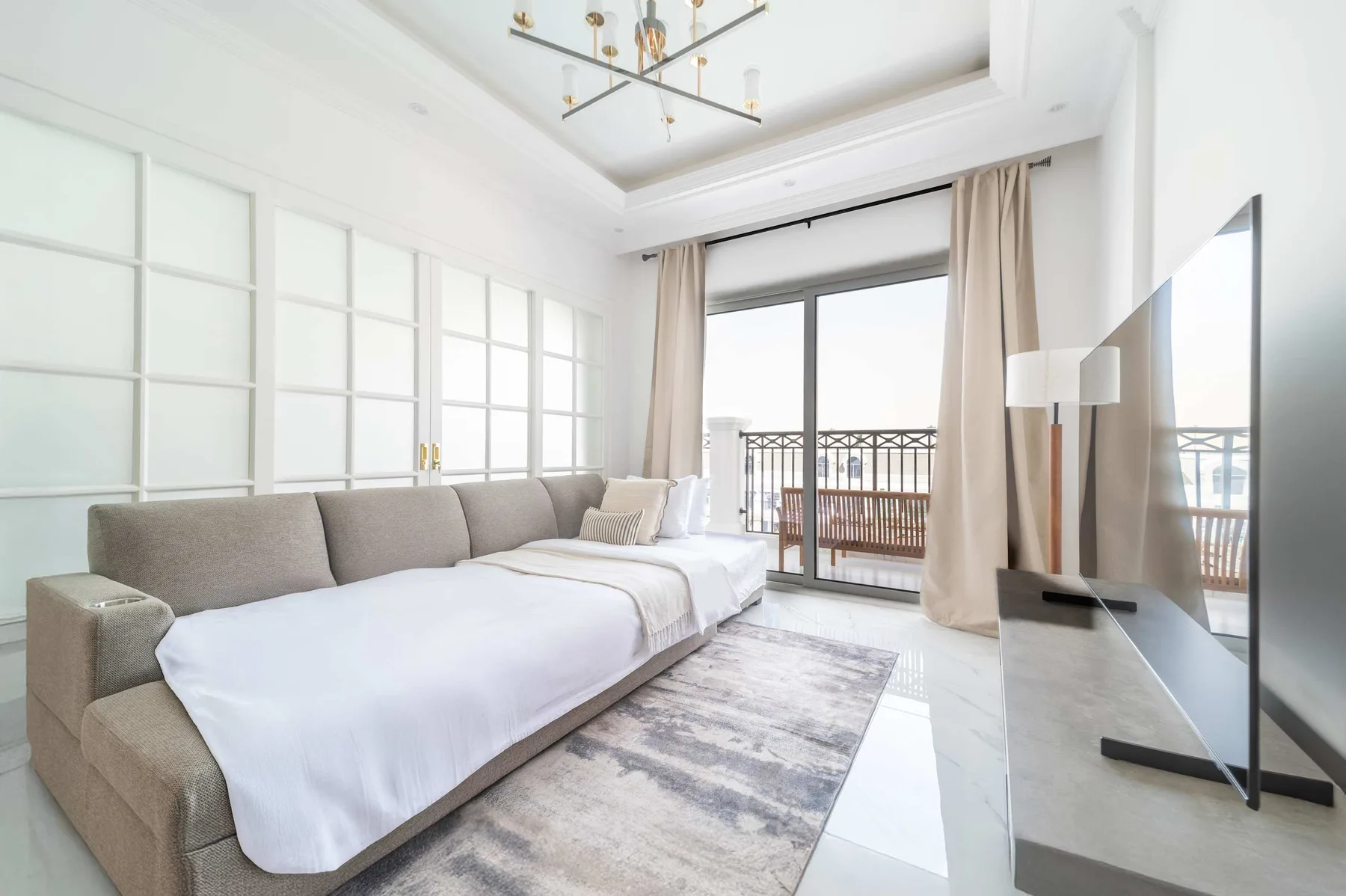 Un dormitorio luminoso con una cama grande, ventanas de suelo a techo y vistas al balcón.