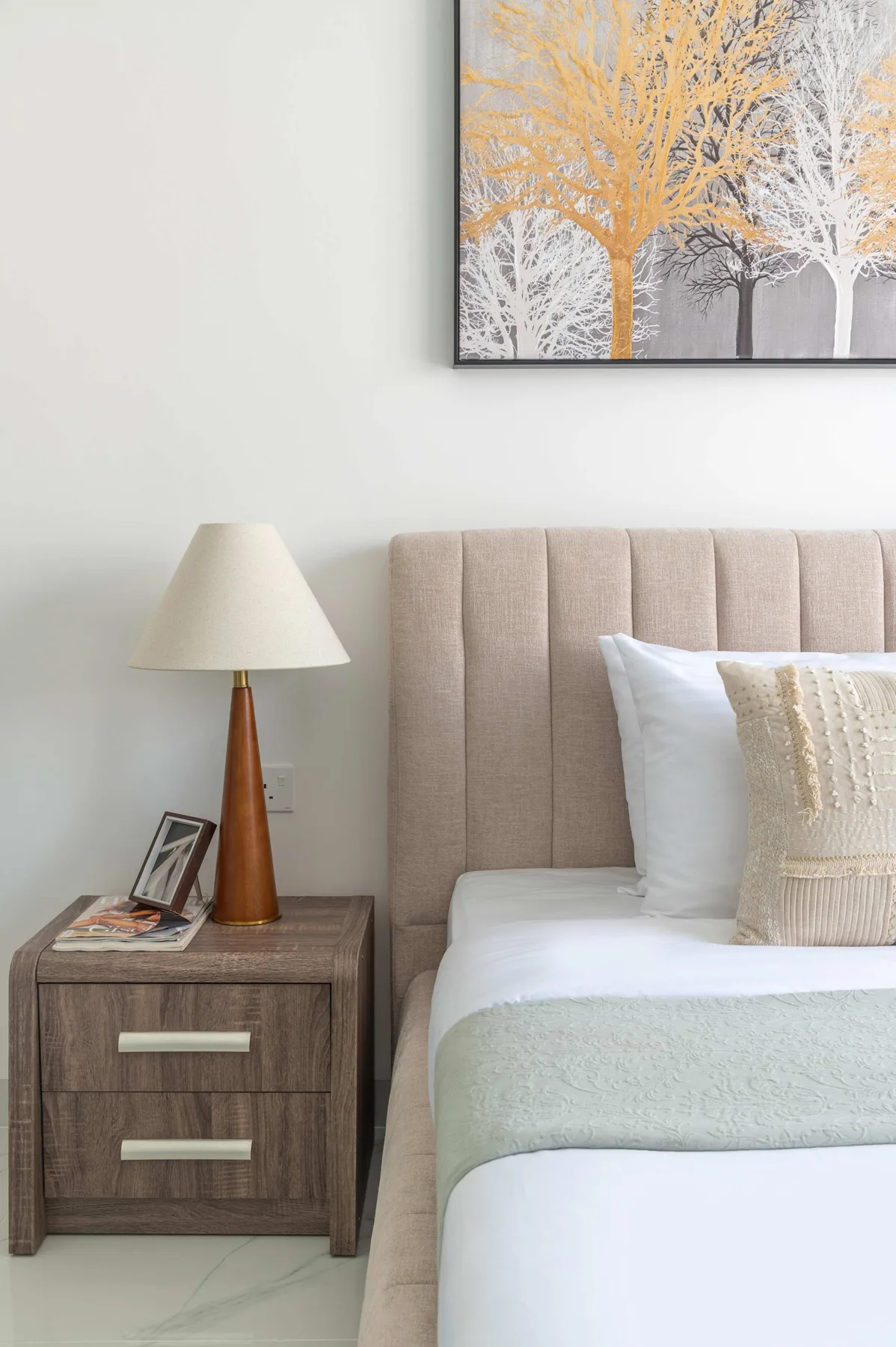 Un dormitorio con una cama ordenada, una mesa de noche y una lámpara.