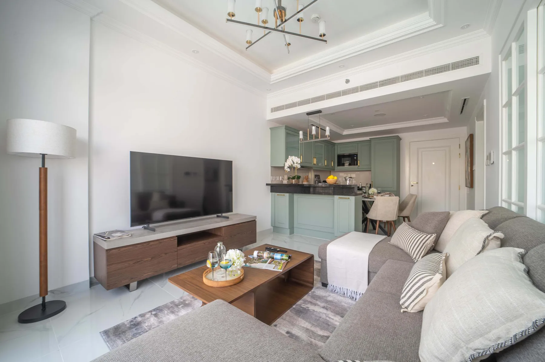 Una sala luminosa con asientos, un televisor y una cocina abierta.