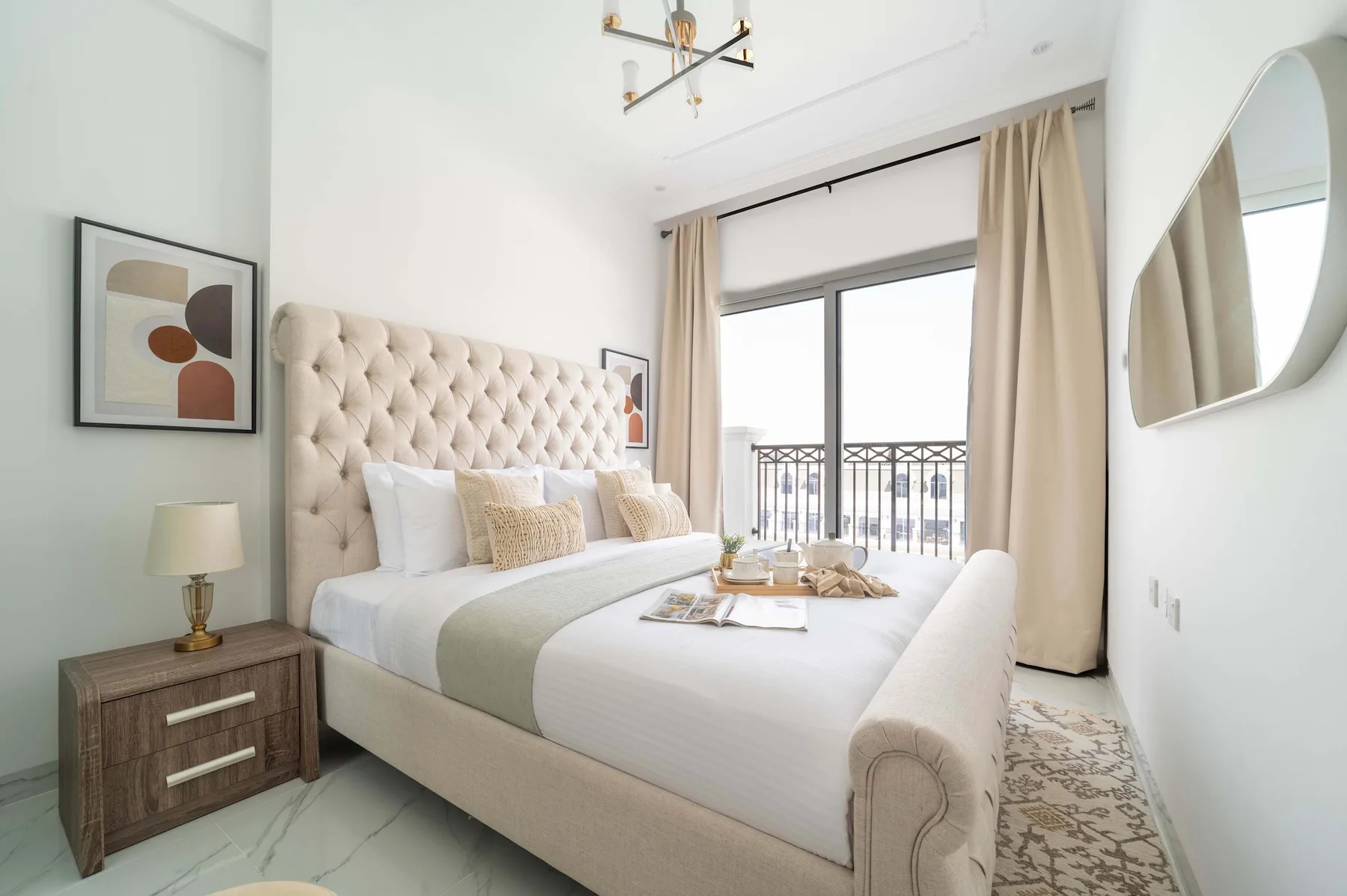 Un dormitorio luminoso con una cama capitoné junto a ventanas altas y una barandilla de balcón.