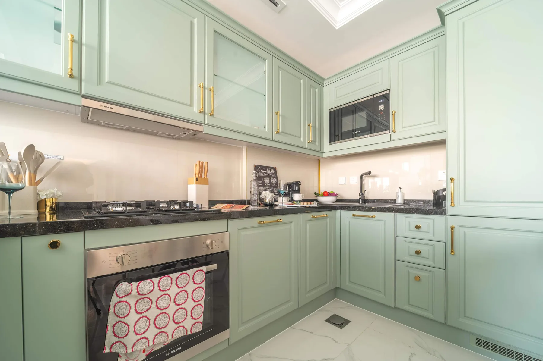 Una cocina verde menta con electrodomésticos integrados y encimeras oscuras.