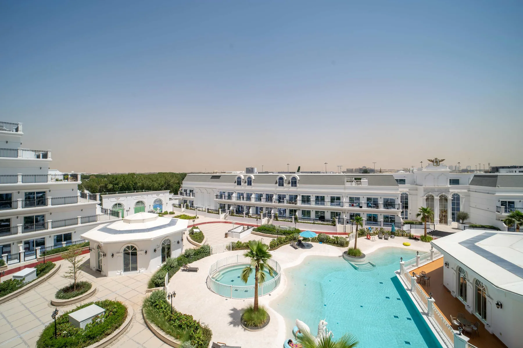 Un patio de complejo turístico cuenta con una piscina turquesa rodeada de edificios blancos.