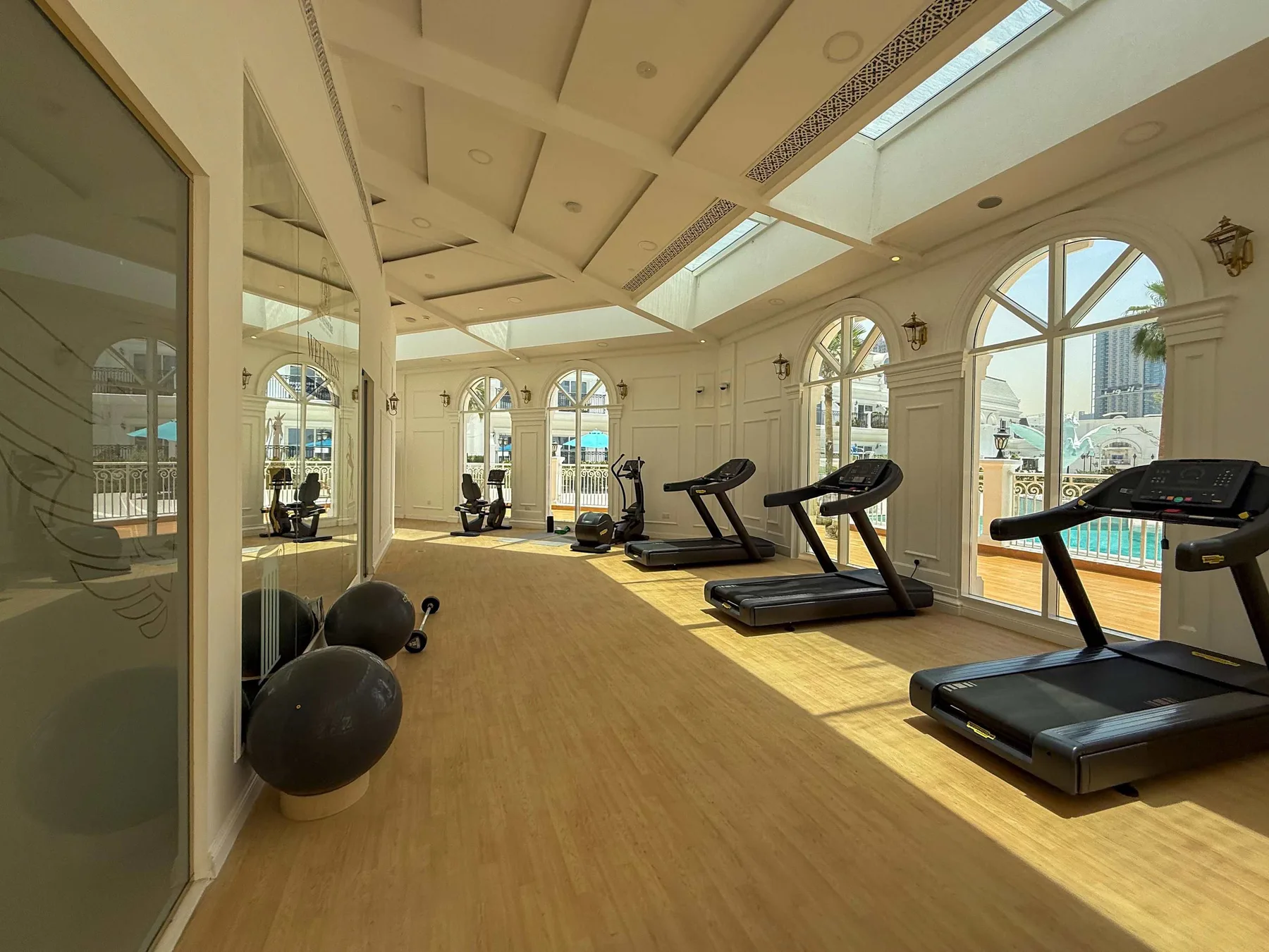 Una sala de ejercicio luminosa con cintas de correr y grandes ventanas arqueadas.